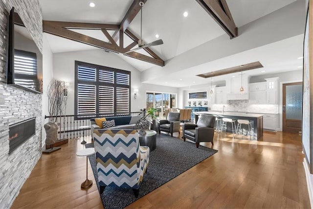 living room with hardwood / wood-style floors, high vaulted ceiling, ceiling fan, a fireplace, and beamed ceiling