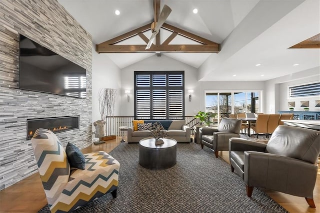 living room with ceiling fan, a stone fireplace, beamed ceiling, high vaulted ceiling, and hardwood / wood-style flooring