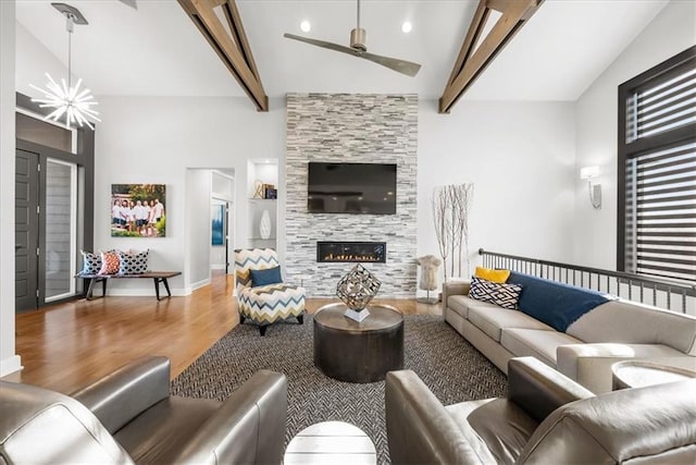 living room featuring a fireplace, ceiling fan with notable chandelier, wood-type flooring, high vaulted ceiling, and beamed ceiling