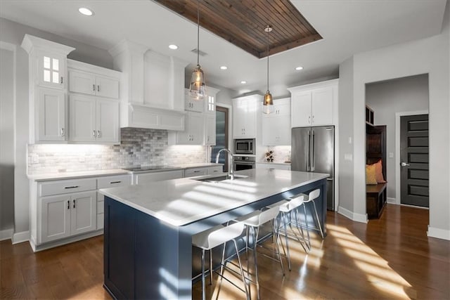 kitchen with white cabinetry, sink, hanging light fixtures, stainless steel appliances, and a center island with sink