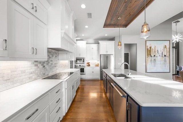 kitchen with hanging light fixtures, dark hardwood / wood-style floors, a kitchen island with sink, white cabinets, and appliances with stainless steel finishes