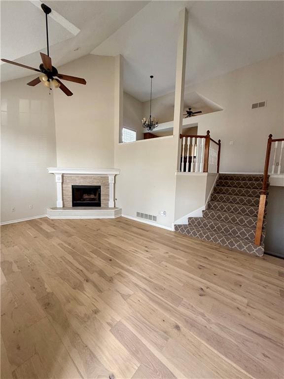 unfurnished living room featuring ceiling fan with notable chandelier, high vaulted ceiling, and light hardwood / wood-style flooring