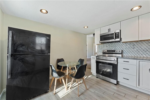 kitchen featuring white cabinets, decorative backsplash, light stone countertops, light hardwood / wood-style floors, and stainless steel appliances