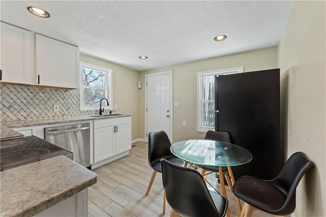 kitchen with white cabinets, sink, light hardwood / wood-style flooring, stainless steel dishwasher, and tasteful backsplash