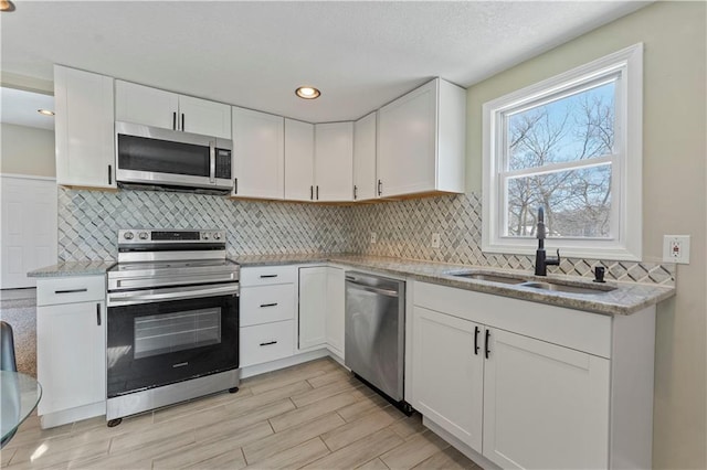 kitchen with a sink, backsplash, appliances with stainless steel finishes, and white cabinetry