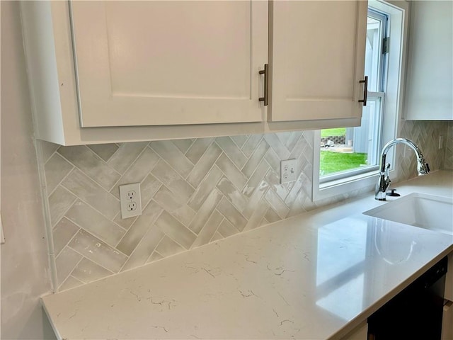 kitchen featuring sink, white cabinetry, black dishwasher, tasteful backsplash, and light stone countertops