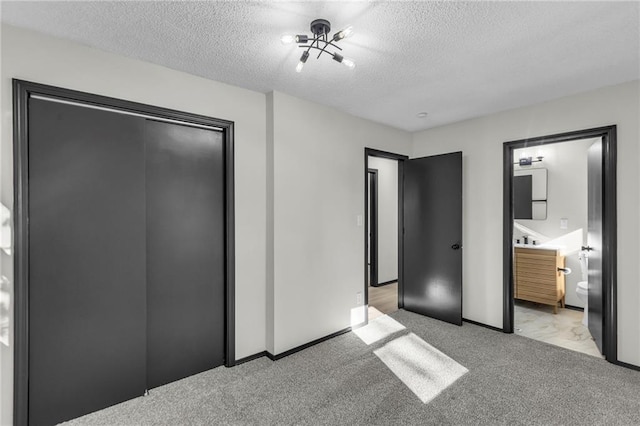 unfurnished bedroom featuring ensuite bathroom, a closet, light colored carpet, and a textured ceiling