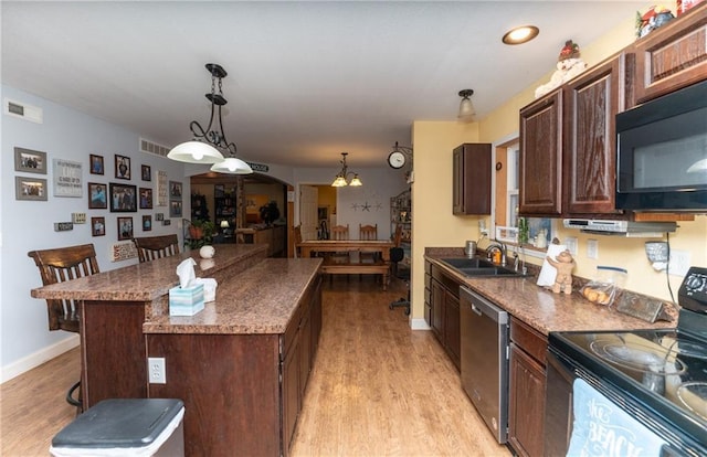 kitchen with a breakfast bar, black appliances, light hardwood / wood-style flooring, a kitchen island, and hanging light fixtures