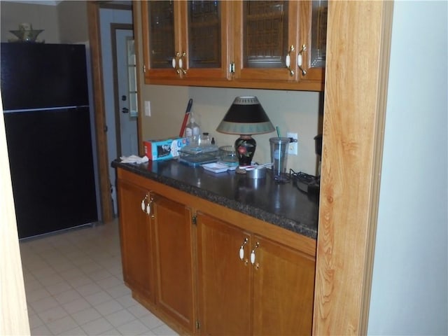 kitchen with light tile patterned floors, black fridge, and dark stone counters