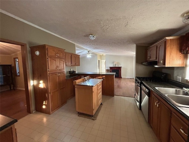 kitchen with sink, crown molding, a textured ceiling, a kitchen island, and appliances with stainless steel finishes