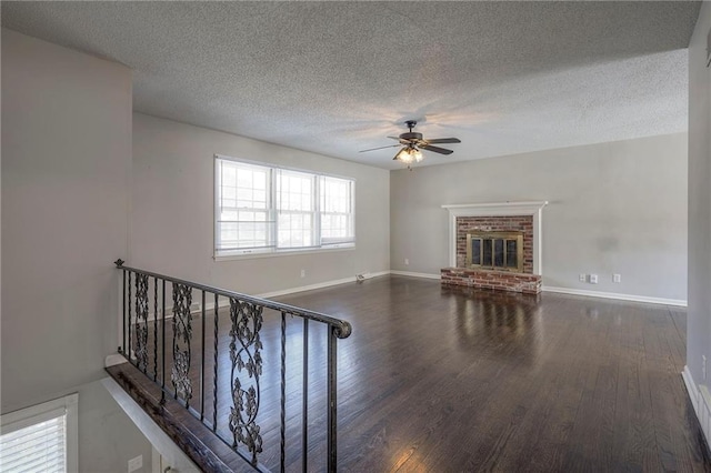 unfurnished living room featuring dark hardwood / wood-style floors, ceiling fan, a fireplace, and a textured ceiling