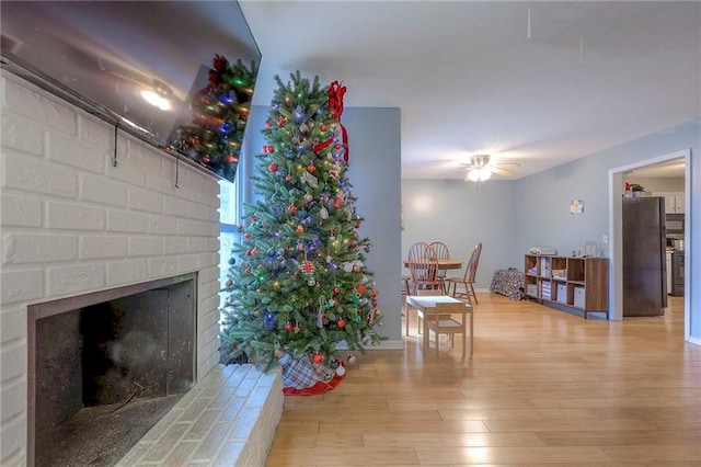 living room with ceiling fan, light hardwood / wood-style flooring, and a brick fireplace