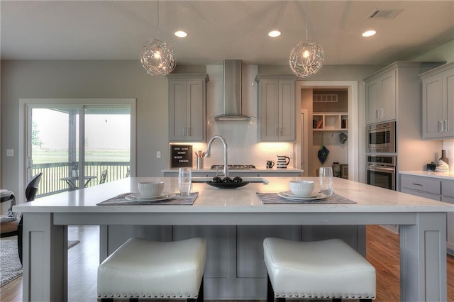 kitchen with wall chimney range hood, gray cabinets, appliances with stainless steel finishes, hanging light fixtures, and a kitchen breakfast bar