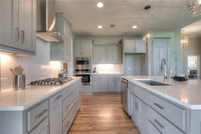 kitchen featuring wall chimney exhaust hood, sink, hanging light fixtures, an island with sink, and stainless steel appliances