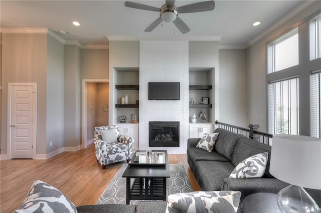 living room featuring built in shelves, crown molding, a large fireplace, wood finished floors, and baseboards