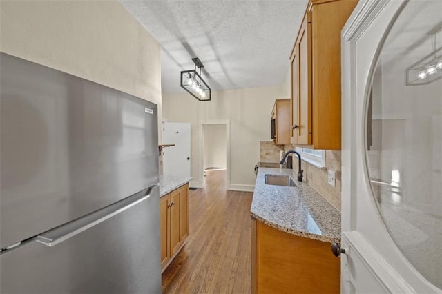 kitchen featuring white refrigerator, sink, light stone countertops, light hardwood / wood-style floors, and stainless steel refrigerator