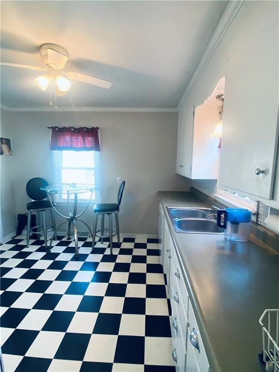 kitchen featuring ceiling fan, sink, white cabinets, and ornamental molding