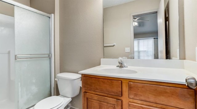 bathroom featuring ceiling fan, vanity, a shower with shower door, and toilet