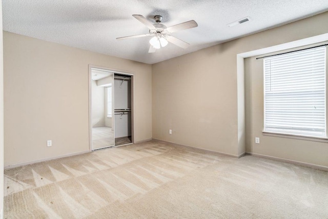 unfurnished bedroom featuring a textured ceiling, light colored carpet, a closet, and ceiling fan