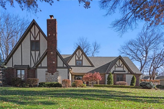 tudor-style house featuring brick siding, stucco siding, a chimney, and a front yard