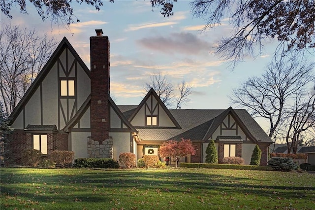 tudor house featuring brick siding, stucco siding, a chimney, and a lawn