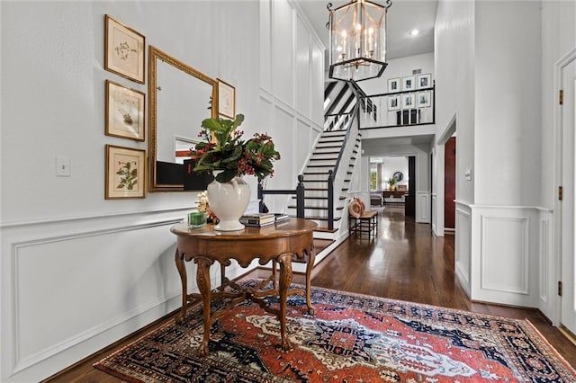 entryway with stairs, a decorative wall, dark wood-style flooring, and a chandelier