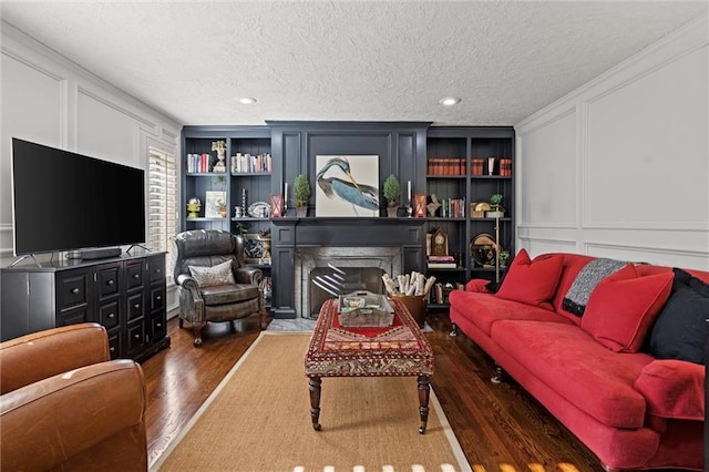 living room featuring built in features, a fireplace, wood finished floors, a decorative wall, and a textured ceiling