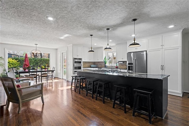 kitchen featuring a kitchen island, white cabinetry, appliances with stainless steel finishes, decorative backsplash, and dark wood-style flooring