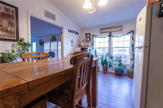 dining space featuring hardwood / wood-style floors, vaulted ceiling, and ornamental molding