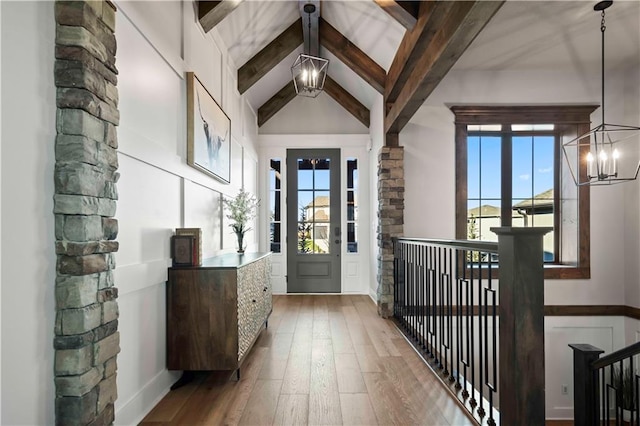 foyer entrance featuring plenty of natural light, beamed ceiling, an inviting chandelier, and hardwood / wood-style flooring