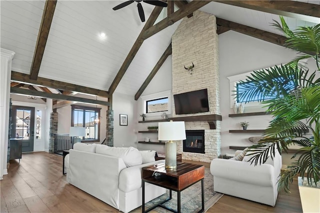 living room featuring high vaulted ceiling, hardwood / wood-style flooring, ceiling fan, a fireplace, and beamed ceiling