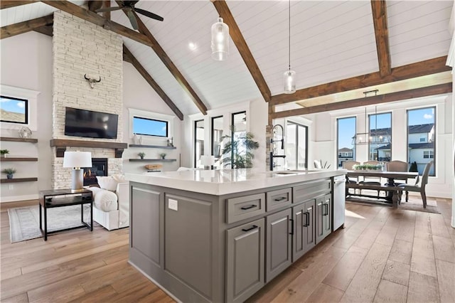 kitchen with gray cabinetry, a center island with sink, high vaulted ceiling, light hardwood / wood-style flooring, and hanging light fixtures