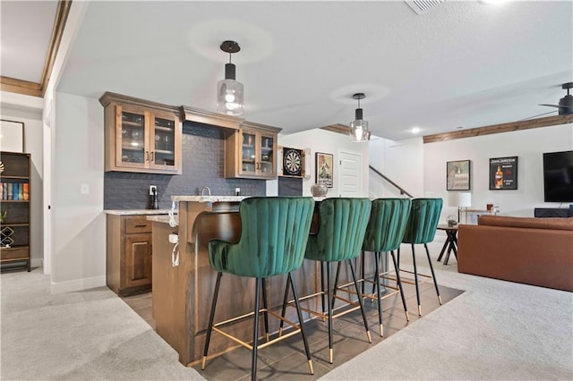 bar featuring ceiling fan, light stone counters, backsplash, pendant lighting, and light colored carpet