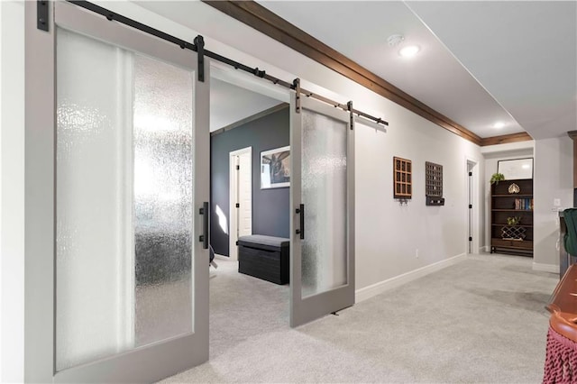 hall with a barn door, crown molding, and light carpet