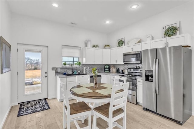 kitchen with stainless steel appliances, decorative backsplash, light wood-style floors, white cabinetry, and a sink