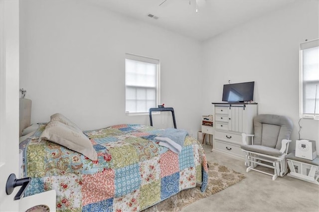 carpeted bedroom featuring multiple windows, visible vents, and a ceiling fan