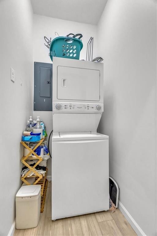 laundry room with light wood-style flooring, laundry area, baseboards, stacked washing maching and dryer, and electric panel