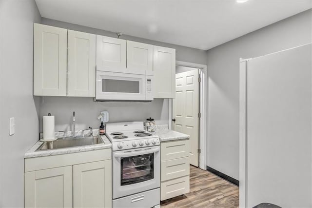 kitchen with white appliances, a sink, white cabinetry, light countertops, and light wood finished floors