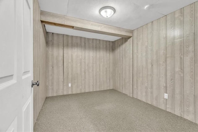 carpeted empty room featuring beam ceiling and wood walls