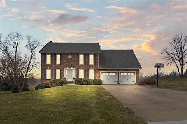 colonial-style house featuring a garage, concrete driveway, brick siding, and a front lawn