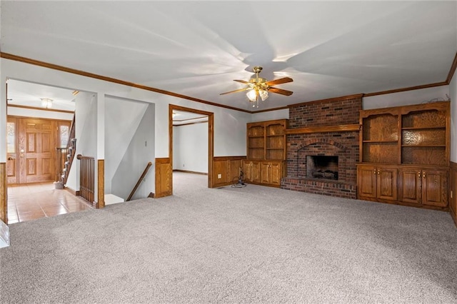 unfurnished living room with wood walls, light carpet, a brick fireplace, ceiling fan, and ornamental molding