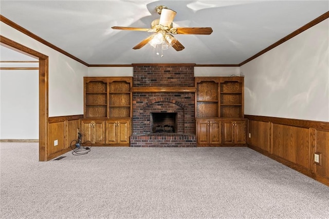 unfurnished living room with light colored carpet, a brick fireplace, ceiling fan, and crown molding