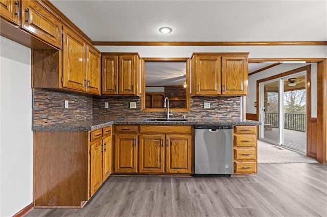 kitchen with dishwasher, sink, dark stone countertops, ornamental molding, and light hardwood / wood-style floors