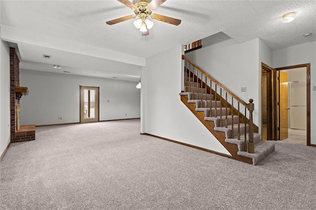 unfurnished living room featuring carpet, ceiling fan, a textured ceiling, and a brick fireplace