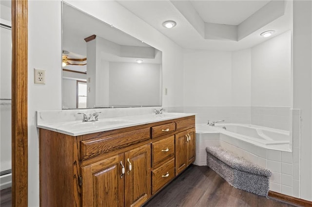 bathroom featuring vanity, a raised ceiling, ceiling fan, hardwood / wood-style floors, and tiled bath