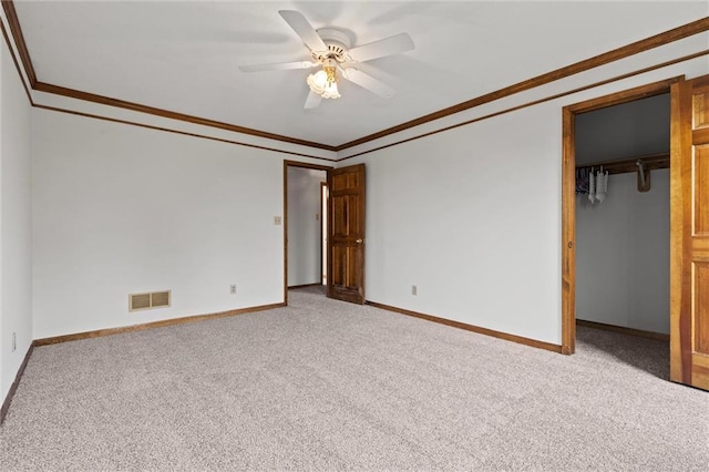 unfurnished bedroom featuring a walk in closet, light colored carpet, ceiling fan, and crown molding