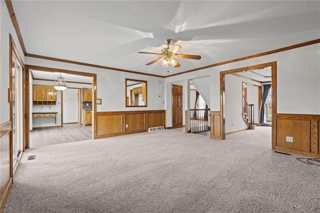 empty room with ceiling fan, ornamental molding, wainscoting, and light colored carpet