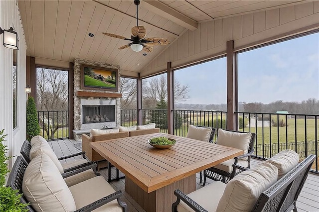 sunroom with vaulted ceiling with beams, ceiling fan, an outdoor stone fireplace, and wooden ceiling