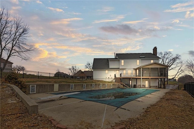 pool at dusk with fence, a sunroom, stairway, a fenced in pool, and a patio area