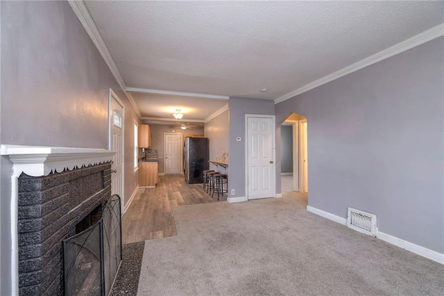 unfurnished living room featuring a fireplace, a textured ceiling, carpet flooring, and ornamental molding